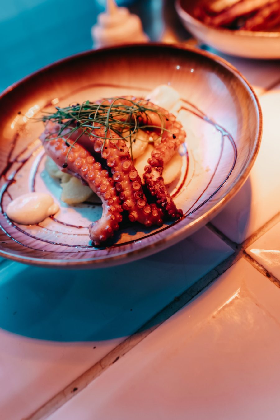 Poulpe grillé sur une purée, avec des pousses vertes, dans une assiette rosée