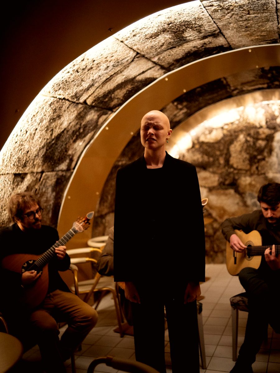 Fadista vêtue de noir chantant sous la voûte de pierre, les deux guitaristes de chaque côté
