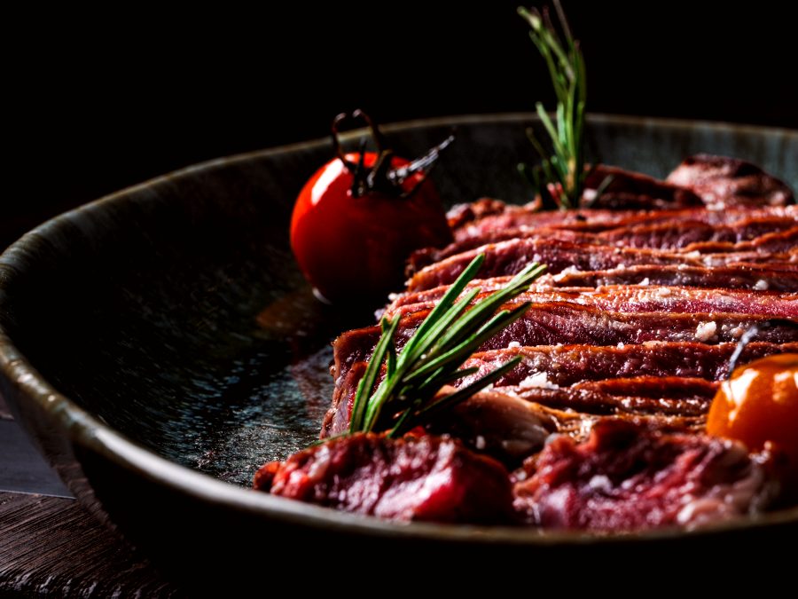 Faux-filet tranché sur un plat en terre cuite, avec romarin et tomate rôtie
